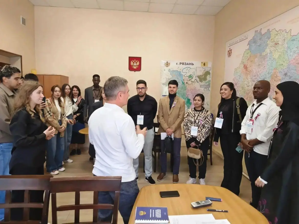 International observers meeting with the chair of the regional Election Commission, with maps of Ryazan in the background.