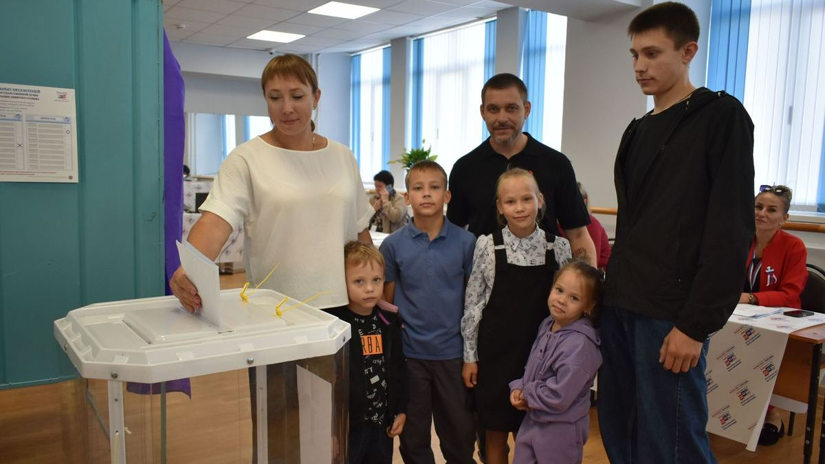 Family with three children placing a ballot in a transparent ballot box.